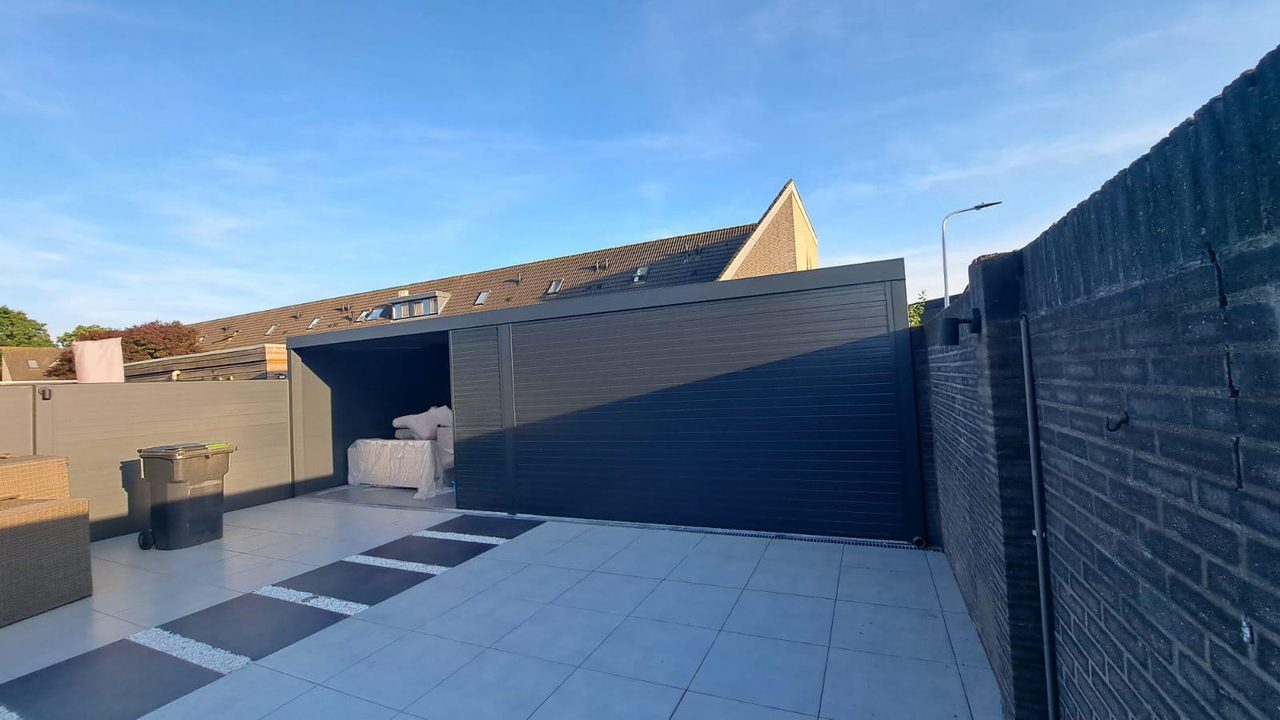 Anthrazitfarbene Aluminiumwand um eine geflieste Terrasse mit Überdachung