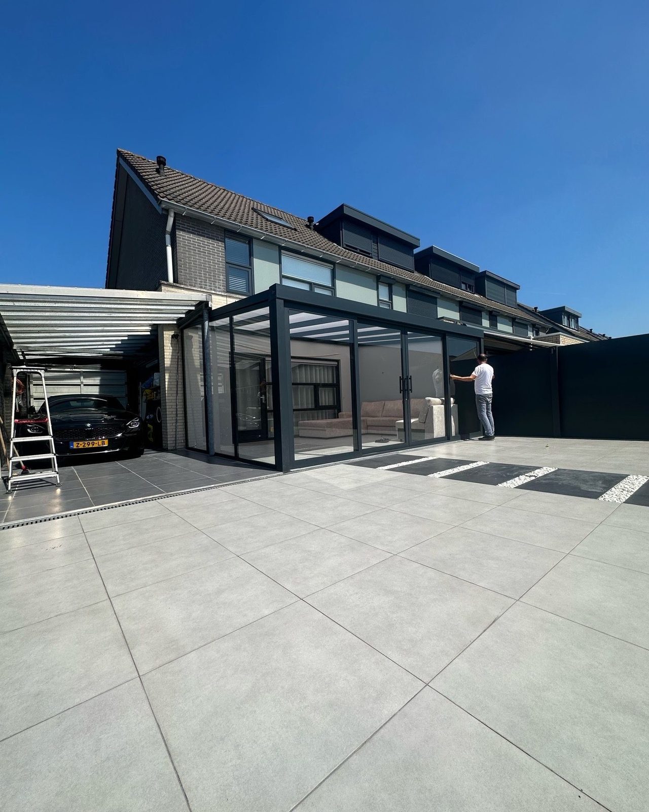 Sommergarten mit Glasschiebewänden neben einer Garage und einer großen gefliesten Terrasse