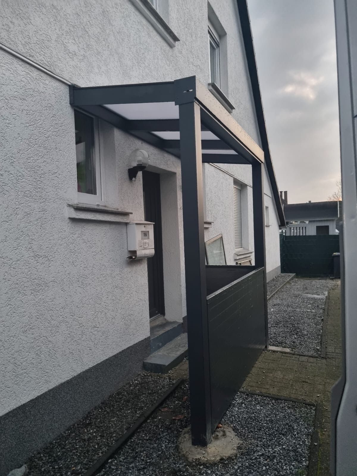 Anthrazitfarbene Eingangsüberdachung an einer weiß verputzten Fassade