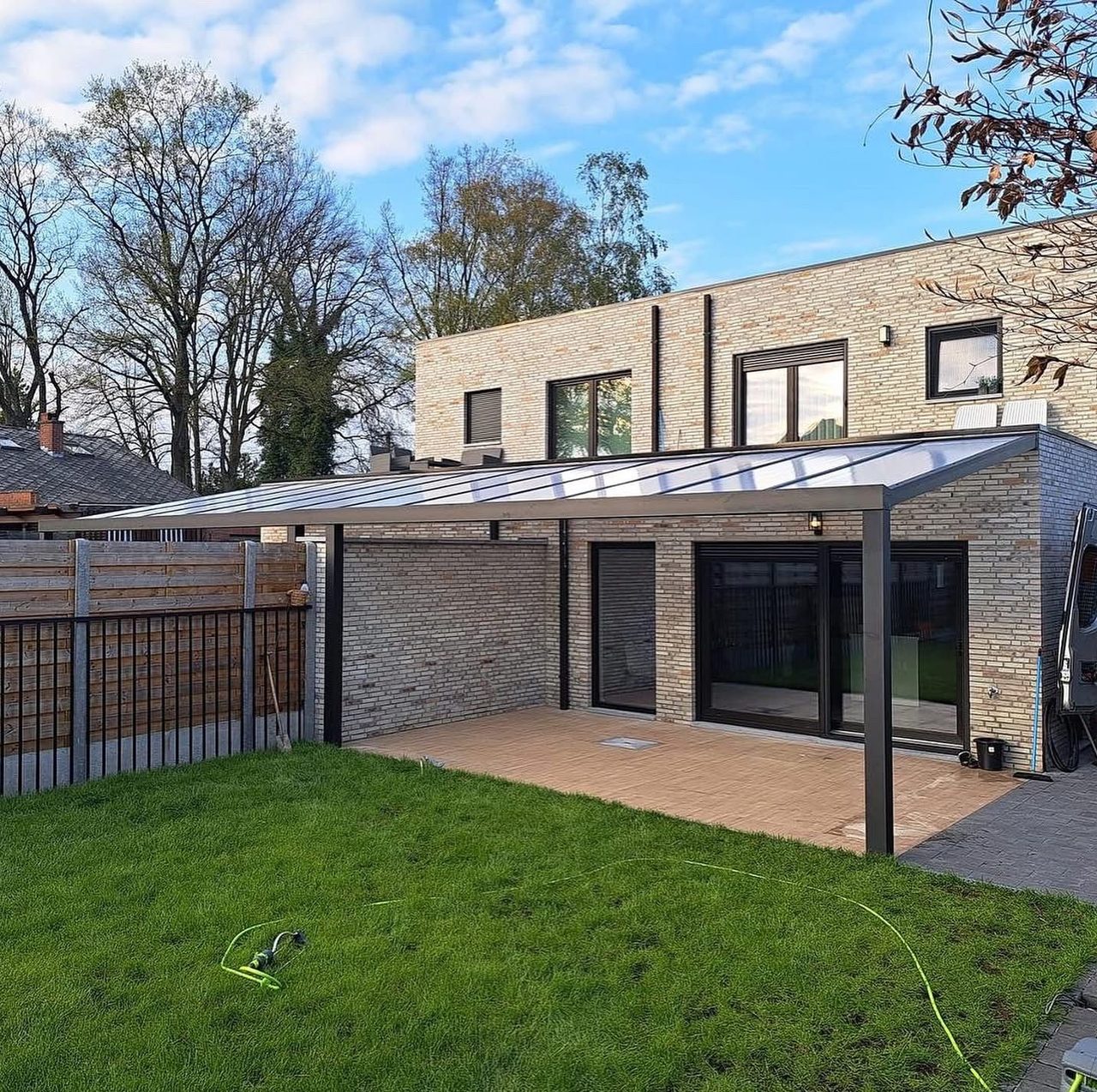 Terrassenüberdachung mit Glasdach an einem modernen Haus mit Rasenfläche
