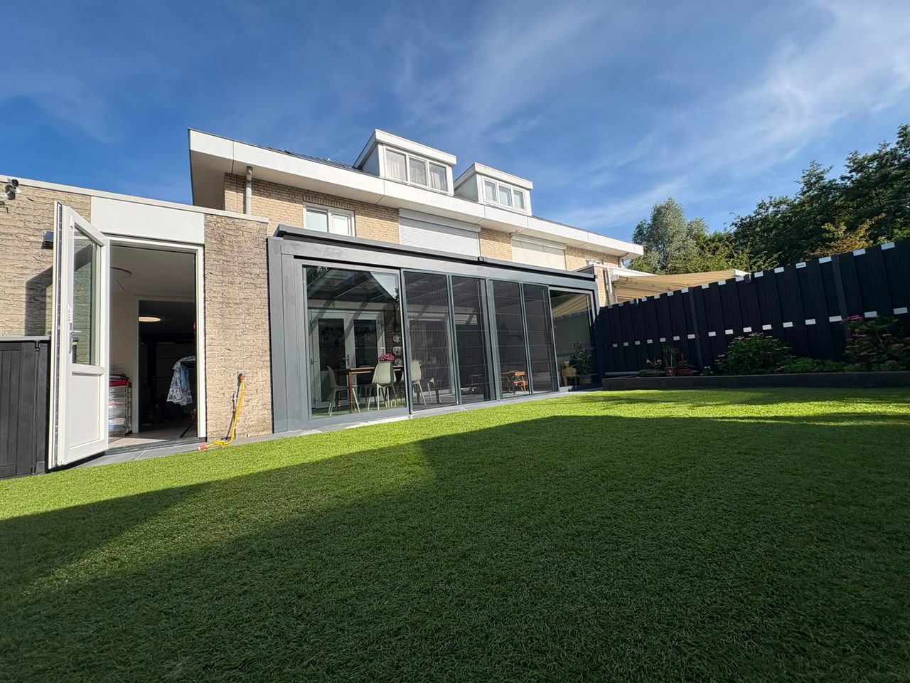 Breiter Sommergarten mit Glasschiebewänden an einem Haus mit großer Rasenfläche