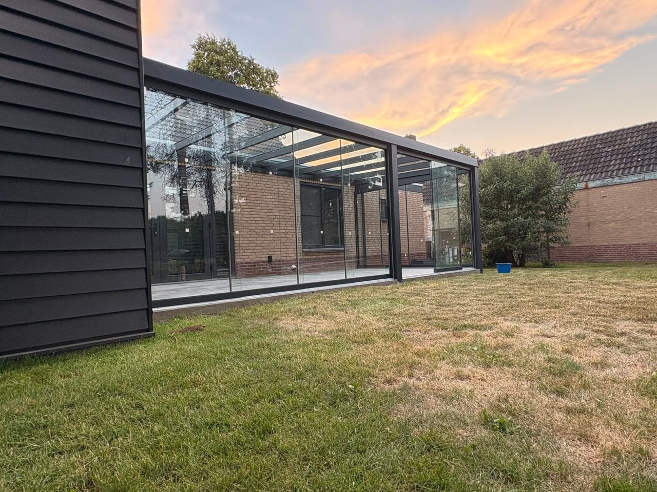 Langer Sommergarten mit Glaswänden und Glasdach bei Sonnenuntergang